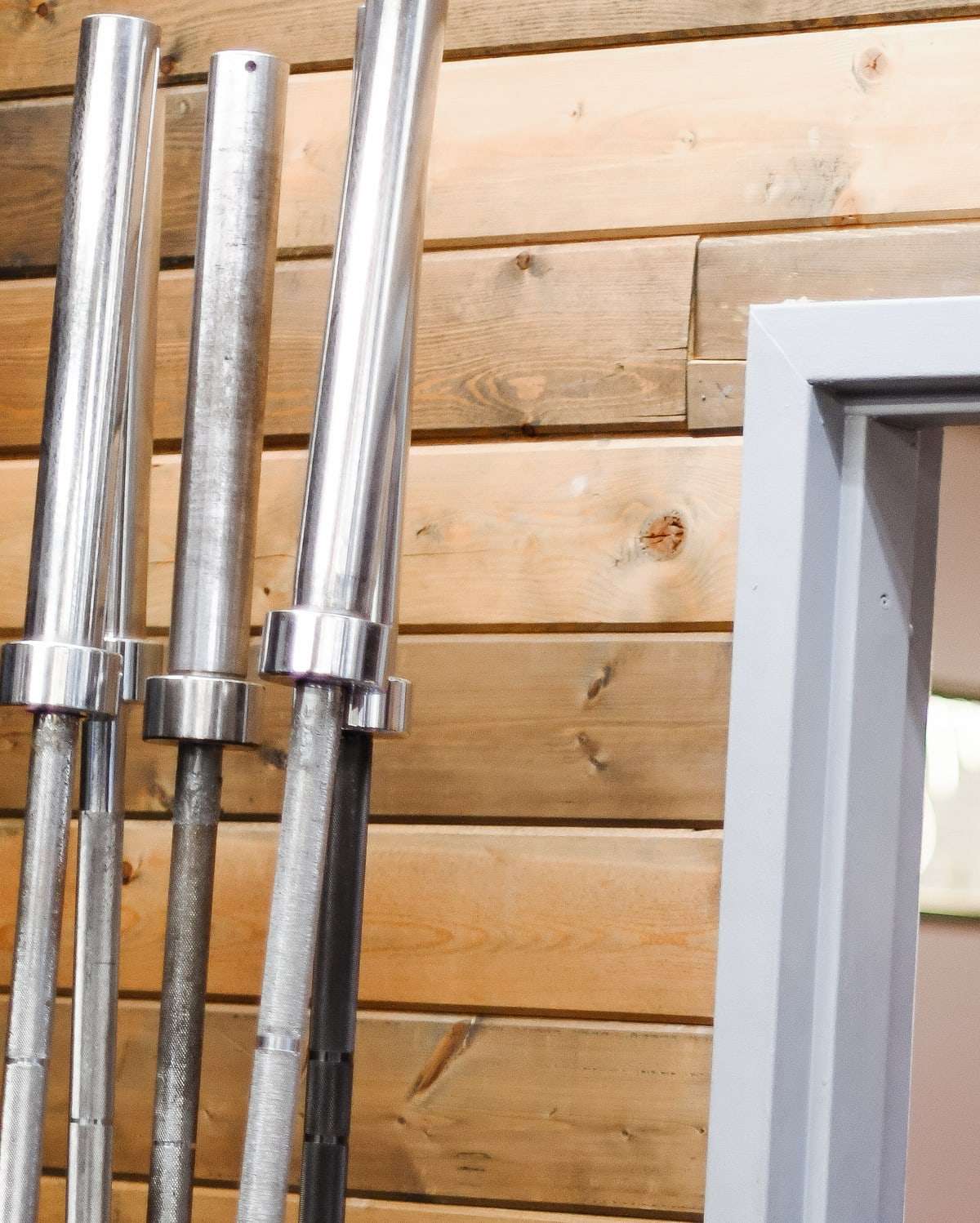 Barbells racked upright against a wall of wood planks.