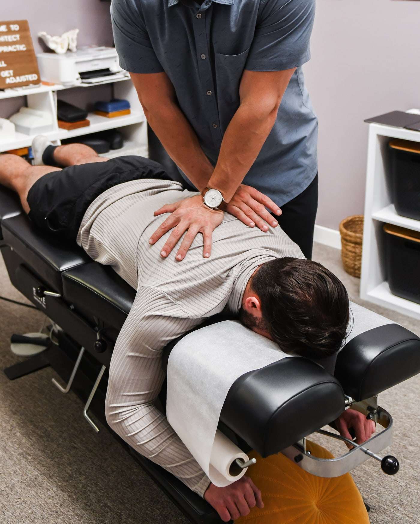 Brent's hands stacked on the mid back of a patient lying face down, wristwatch visible.