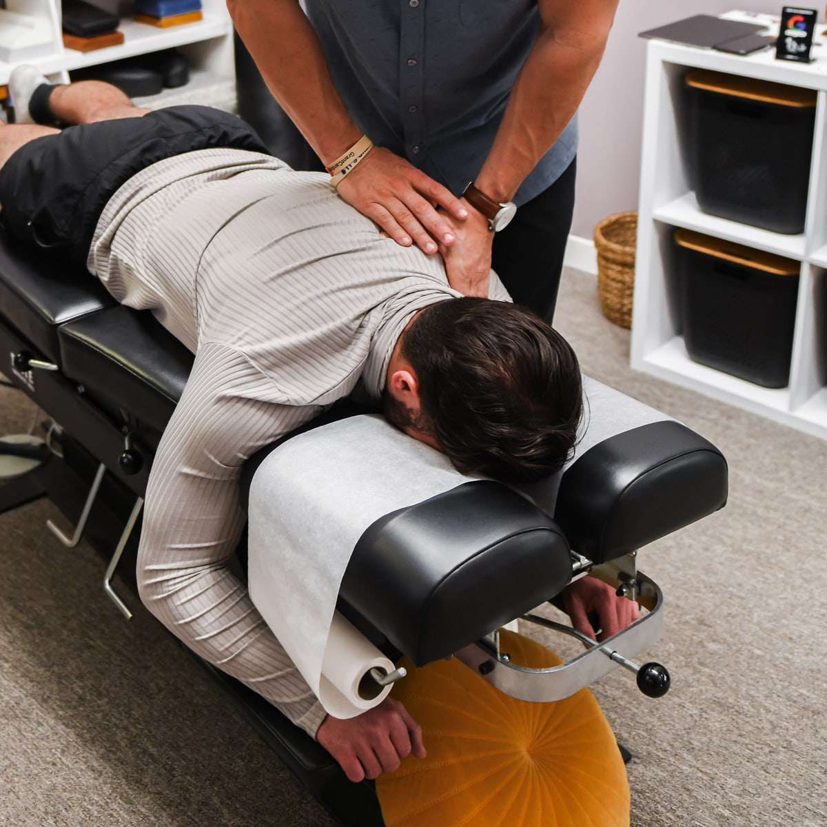 Brent's hands on the mid back of a patient lying face down, a wristwatch visible.